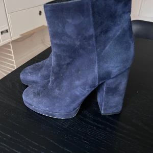 Blå mocka boots novita  - Snygga blå boots i mocka med hög klack. Perfekta för att ge en stilren touch till din outfit. De har en elegant design och är tillverkade i ett mjukt material som ger en lyxig känsla.