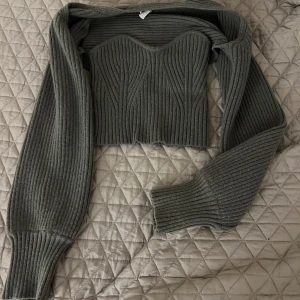 Grå ribbad korsett med ärmar - Snygg grå ribbad korsett  med avtagbara ärmar. Perfekt för en trendig look. Den har en tight passform och är tillverkad i ett mjukt stickat material.