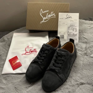Christian Louboutin - Snygga svarta/gråa sneakers från Christian Louboutin med den ikoniska röda sulan. Skorna har en stilren design med snörning och är tillverkade i skinn. Perfekta för den som vill ha en lyxig touch i vardagen. Kvitto, dustbag, shoebox och confirmation card ingår! Obs att det finns små tecken på användning på sulan, därav priset. 