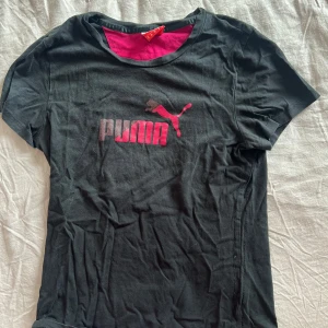Svart t-shirt från Puma - Säljer en svart t-shirt från Puma med rosa logga på bröstet. Den har en normal passform och är kortärmad. Perfekt för både träning och vardag!