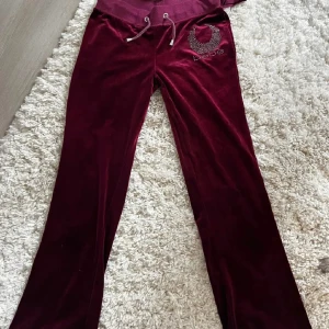 Vinröda mjukisbyxor med strassdetaljer - Säljer ett par supermysiga vinröda mjukisbyxor i sammet. De har en snygg strassdetalj på ena benet och snörning i midjan. Perfekta för en lugn dag hemma eller en avslappnad dag ute. 🩷 I storlek medium men sitter som xs- s. 