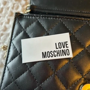 Svart  väska från Love Moschino - Säljer en superfin svart  väska från Love Moschino. Den har en snygg kedjerem och ett stort Love Moschino-märke på framsidan. Perfekt för både vardag och fest! 🖤