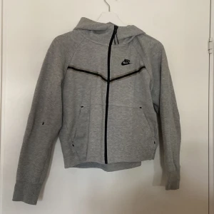 Grå hoodie från Nike - Säljer en snygg grå hoodie från Nike i storlek S. Den har en dragkedja framtill och en klassisk Nike-logga på bröstet. Perfekt för både träning och vardag. Hoodien är i bra skick och superbekväm att ha på sig. Nypris ca. 900kr.
