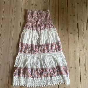 Blommig långklänning med spetsdetaljer - Säljer en superfin långklänning med blommigt mönster i rosa, lila och orange. Klänningen har vita partier och vackra spetsdetaljer längst ner. Perfekt för sommarens fester eller en mysig dag på stan. Den har en bekväm passform och väldigt stretchig 💕är alldeles för kort för mig , jag är 175cm. står inte storlek eller märke men skulle säga att den är xs-s