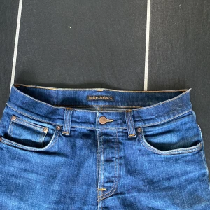 Nudie jeans 👖  - Säljer ett par snygga blå jeans från Nudie Jeans. De har en klassisk femficksdesign med orange sömmar och en bekväm passform. Jeansen är i bra skick. De har en knappgylf och är tillverkade i slitstarkt denim. Nypris är 1600kr