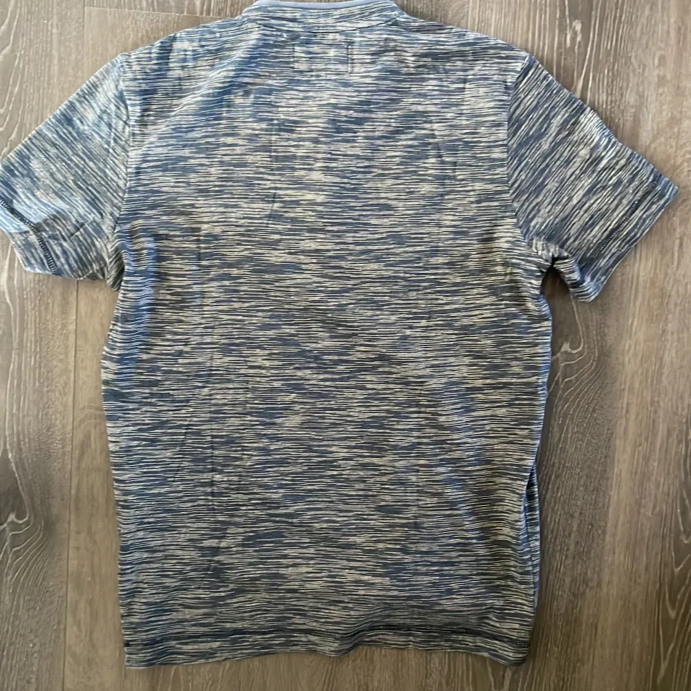 Säljer en snygg blå randig t-shirt från Tom Tailor. Den har korta ärmar och en knappdetalj framtill som ger en stilren look. Perfekt för både vardag och avslappnade tillfällen. Materialet känns mjukt och bekvämt. Aldrig använt.. T-shirts.