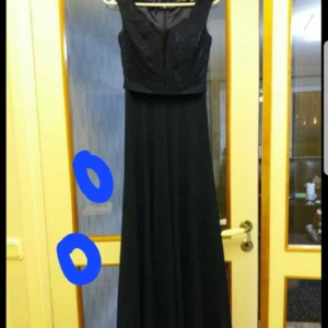 Svart långklänning - Elegant svart långklänning med ärmlös design och spetsdetaljer upptill. Perfekt för formella tillfällen med en klassisk och tidlös stil. 36/38