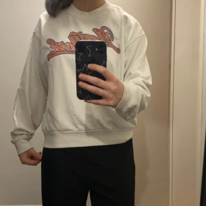 Vit sweatshirt med tryck - Säljer en vit sweatshirt med ett färgglatt tryck på bröstet. Tröjan har långa ärmar och en avslappnad passform, perfekt för en casual look. Den är bekväm och stilren, idealisk för vardagsbruk.