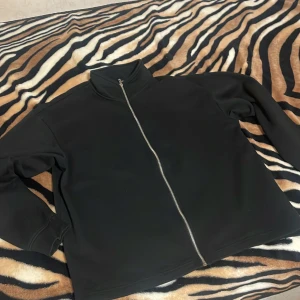 Svart jacka med dragkedja - Snygg svart jacka med dragkedja framtill. Perfekt för en stilren look. Jackan har långa ärmar och en hög krage.