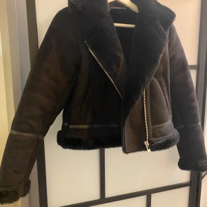 Svart jacka med pälsdetaljer - Snygg svart jacka med pälsdetaljer och dragkedja. Jackan har en modern design med en krage och muddar i päls, vilket ger en lyxig känsla. Perfekt för kyligare dagar.