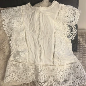 Vit spettopp  - Charmig vit klänning med vackra spetsdetaljer och korta ärmar. Perfekt för somriga dagar med sin luftiga design då man inte blir för varm i den. Den har en öppen rygg och är super trendig! Köpte den second hand och lappen är borta så vet varken vilket märke det är eller storlek, men passar mig som har storlek xs-s 
