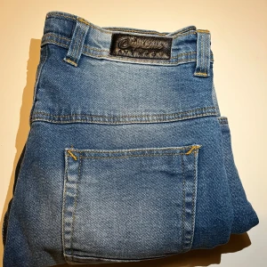 Blå jeans med slitningar - Snygga blå jeans med slitningar på framsidan för en trendig look. De har en klassisk femficksdesign och en bekväm passform. Perfekta för en avslappnad stil.