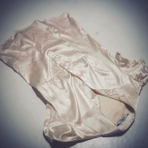 Gräddvit blus i satin - Elegant och stilren blus i gräddvit. Materialet är av satin och väldigt behagligt att bära. Plagget är perfekt till vardags eller till fest.