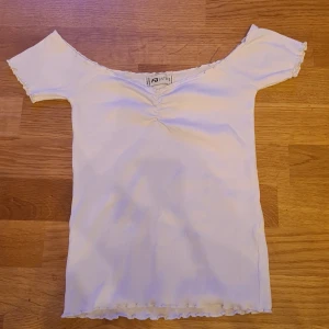 Vit ribbad topp från Sisters Point - Snygg vit ribbad topp från Sisters Point med korta ärmar och en söt rynkdetalj framtill. Toppen har en offshoulder-design och vågiga kanter.