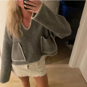 Grå tröja med vita detaljer - Mysig grå tröja med vita kantdetaljer och två framfickor. Tröjan har en v-ringad hals och långa ärmar, perfekt för kyligare dagar.Köpte för 500kr men säljer för 350kr🩷