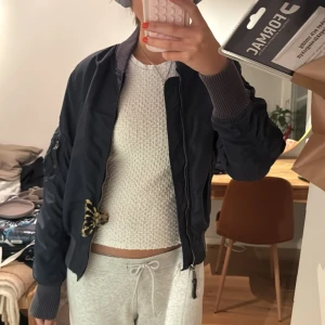 Mörkblå  bomberjacka - Snygg mörkblå bomberjacka med dragkedja och ribbade muddar. Perfekt för en casual look. Jackan har en klassisk bomberstil med en liten detalj på ärmen.