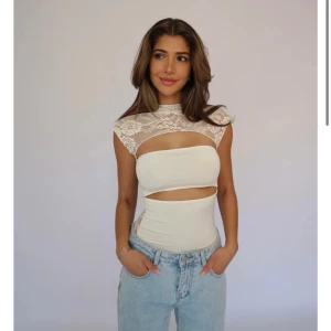 Krämfärgad Lucy Lace Top - Snygg krämfärgad topp med spetsdetaljer och cut-out design. Toppen har en tight passform och är ärmlös med en elegant spets runt halsen och axlarna. Den är mer beige än vad man ser på bilderna. Har tagg kvar, ej använts.