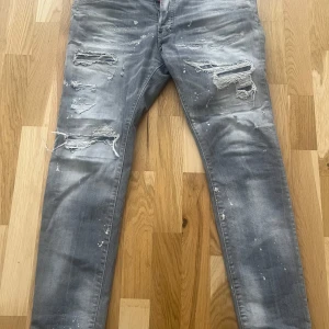 Dsquared2 - Säljer ett par dsquared jeans med slitna detaljer och färgstänk. De har en modern look med flera revor på framsidan och en bekväm passform. Perfekta för en avslappnad stil.