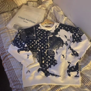 Vit och blå sweatshirt från Louis Vuitton - Säljer en snygg vit och blå sweatshirt från Louis Vuitton med ett unikt mönster. Tröjan har långa ärmar och en bekväm passform. Perfekt för dig som vill ha något stilrent och exklusivt i garderoben. Modellen är 182 och väger 70 kg. Skicket är 10/10 och allt og ingår, storlek S men sitter som en M