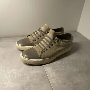 Lanvins Byen sökes  - Snygga beige sneakers med grå tåhätta och snörning. Skorna har en stilren design med en kombination av mocka och syntetmaterial. Perfekta för en avslappnad stil. Såklart äkta säljes för 1300 pga in box och så för det försvann i flyt. Priset är absolut inte hugget I sten