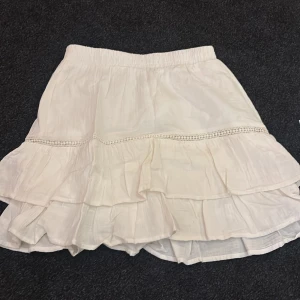 Vit kjol från Vila - Charmig vit kjol från Vila med volanger och elastisk midja. Knappt använd 