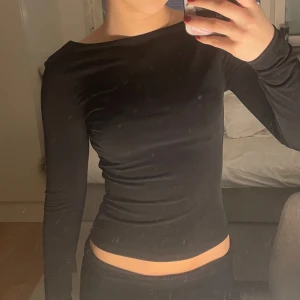 Svart långärmad topp utan rygg - Snygg svart långärmad topp med en tight passform och öppen rygg. Perfekt för en stilren look.