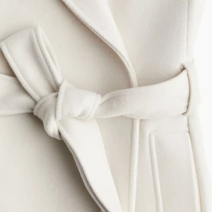 Vit/beige kappa från H&M - Elegant vit kappa från H&M med knytbälte i midjan. Den har en klassisk krage och långa ärmar, perfekt för kyligare dagar. Stilren design som passar till många tillfällen. Aldrig använd 