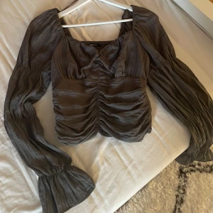Grå blus från Gina Tricot - Säljer en elegant grå blus från Gina Tricot med långa puffärmar och rynkade detaljer framtill. Använd bara en gång✨. 