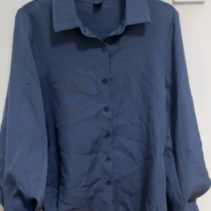 Blå långärmad skjorta - Snygg blå skjorta med långa ärmar och knappar framtill. Perfekt för en stilren look. Användes när jag var utomlands i somras men har inte använt den sen dess. 