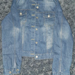 Blå jeansjacka - Snygg blå jeansjacka med klassisk design och knappar framtill. Jackan har två bröstfickor med knappstängning och långa ärmar. Perfekt för en avslappnad stil.