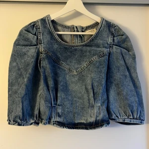 Blå jeansblus från Lindex - Blå jeansblus från Lindex med trekvartsärmar och dragkedja i ryggen. Blusen har en rund halsringning och puffiga ärmar. Endast testad men passade tyvärr inte. 