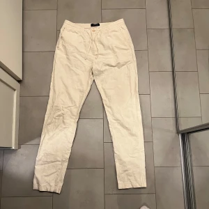 Beige linnebyxor med snörning - Snygga beige linnebyxor med elastisk midja och snörning för en bekväm passform. Perfekta för en avslappnad look. Byxorna är från Scotch&Soda och är i storlek W32 L34