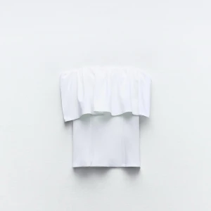 Vit offshoulder topp - Snygg vit offshoulder topp med volangdetaljer. Perfekt för sommarens varma dagar. Den är axelbandslös och har en luftig passform som ger en stilren look.