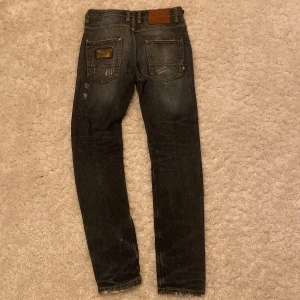 Jeans från Adrian Hammond - Snygga jeans från Adrian Hammond med slitna detaljer och en cool tvätt. De har en klassisk femficksdesign och en metallplatta med logotyp på bakfickan. Perfekta för en avslappnad stil.