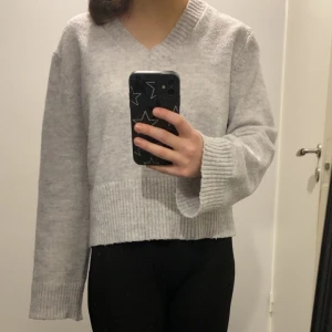 Grå stickad tröja med v-ringning - Säljer en supermysig grå stickad tröja med v-ringning. Den har långa ärmar och en ribbad kant vid ärmslut och nederkant. Perfekt för höst och vinter! 🧶
