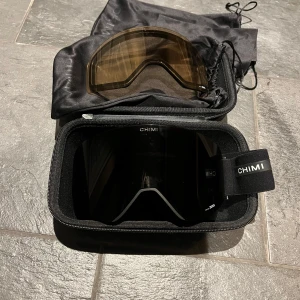 CHIMI Ski Goggles O2 Black - Snygga och funktionella skidglasögon från CHIMI i modellen O2. De har en svart design med Zeiss-linser för optimal sikt. Justerbart band med CHIMI-logga och kommer med ett praktiskt fodral och extra lins. Notera att dessa är den ”dyrare” modellen och där med priset.