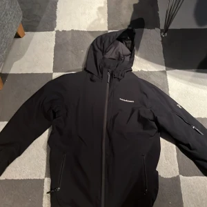 Svart jacka från Peak Performance - Säljer en stilren svart jacka från Peak Performance. Jackan har en huva och dragkedja framtill samt praktiska fickor med dragkedjor. Perfekt för en sportig look. Denna är perfekt för skidåkning och är varmare än majoriteten av jackor. Knappt använd och i toppen bra skick. Nypris 2000 kr