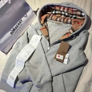 Grå hoodie från Burberry - Säljer en stilren grå hoodie från Burberry med klassiskt rutigt mönster i huvan. Tröjan har dragkedja framtill och är perfekt för en avslappnad look. Passar bra till både jeans och joggers.