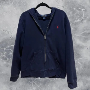 Mörkblå hoodie från Polo Ralph Lauren - Säljer en snygg mörkblå hoodie från Polo Ralph Lauren med dragkedja och det klassiska röda logotypen på bröstet. Perfekt för en avslappnad stil. Den har en bekväm passform och är tillverkad i mjukt material. Passar 160-175 cm (XS-S)