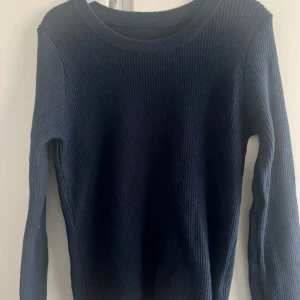 Mörkblå ribbad tröja - Säljer en stilren mörkblå ribbad tröja med långa ärmar. Perfekt för kyligare dagar och enkel att matcha med olika outfits. Tröjan har en klassisk rund halsringning och är gjord i ett mjukt material.