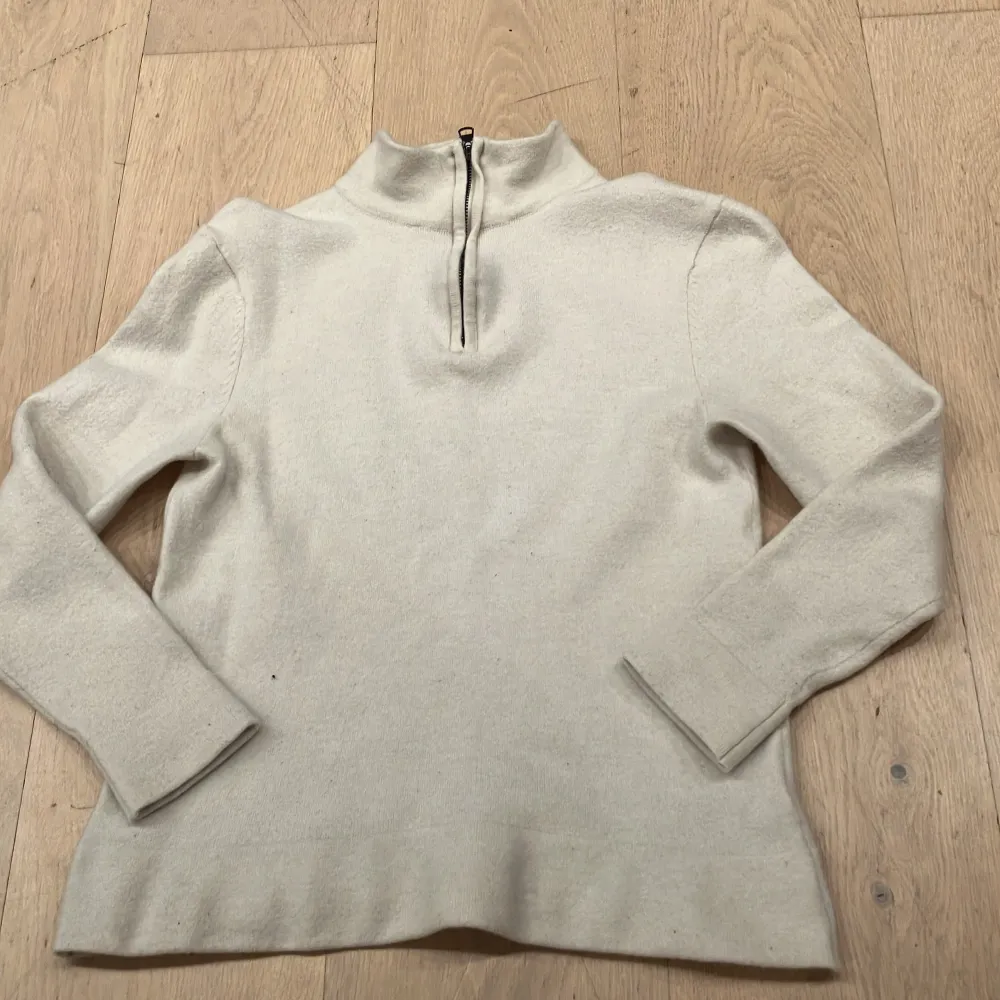 Säljer en stilren beige tröja i merinoull från These Glory Days. Tröjan har en dragkedja vid halsen och långa ärmar, perfekt för kyligare dagar. Den är mjuk och bekväm, vilket gör den till ett utmärkt val för både vardag och mer uppklädda tillfällen. Den är dock lite mindre än s då den har krympt i tvätten.. Neuletakit & Villapaidat.