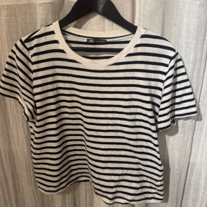 Randig t-shirt från Zara - Säljer en klassisk svartvit randig t-shirt från Zara. Den har en rund halsringning och korta ärmar, perfekt för en avslappnad stil. Tillverkad i ett mjukt och bekvämt material.