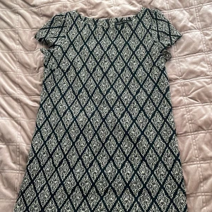Mönstrad klänning från Zara Woman - Snygg klänning från Zara Woman med ett elegant mönster i svart och beige. Klänningen har korta ärmar och en klassisk passform som passar perfekt för olika tillfällen som fester. Tillverkad i Turkiet.