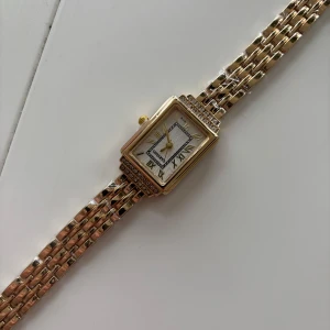 Guldig klocka - Superfin guldig klocka med rektangulärt urtavla. Helt ny och aldrig använd. Har plast kvar runt armbandet. Oklart vart den är ifrån då jag fick den i present. 