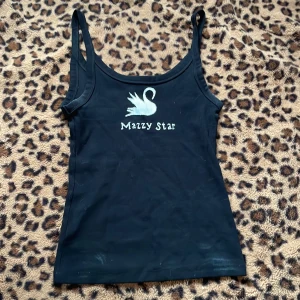 Svart linnetopp med tryck - Snygg svart linnetopp med ett målat tryck av en svan och texten 'Mazzy Star' på framsidan. Perfekt för en avslappnad stil med smala axelband och en figurnära passform. Vita fläckar lite överallt 