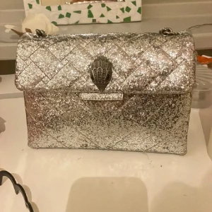 Glittrig silverväska med kedja - Snygg glittrig silver väska från kurt geiger❤️ Man kan ha den tvärs över bröstet eller runt axeln. Lägger upp annonsen igen och det är 700kr som gäller  