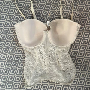 Vit spetskorsett - Vit/beige korsett topp med justerbara band som även går att ta av. Har slitage som ses på bilderna. Storlek 75C/M. !KÖP ENDAST VIS POSTNORD!