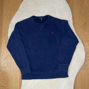 Mörkblå sweatshirt från Polo Ralph Lauren - Säljer en stilren mörkblå sweatshirt från Polo Ralph Lauren med det klassiska röda logotypen broderad på bröstet. Tröjan har långa ärmar och en rund halsringning. Perfekt för en avslappnad look, Storleken är 170.