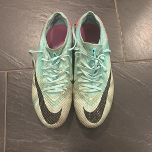 Nike fotbollsskor i turkos och rosa - Säljer ett par Nike fotbollsskor i turkos och rosa med svart swoosh. Skorna har snörning och en iögonfallande design med rosa detaljer på hälen. Perfekta för fotbollsplanen med sina dobbar för bra grepp.