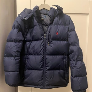 Mörkblå dunjacka från Polo Ralph Lauren - Säljer en snygg mörkblå dunjacka från Polo Ralph Lauren. Den är nästan oanvänd och i väldigt bra skick. Bara att höra av er vid frågor!